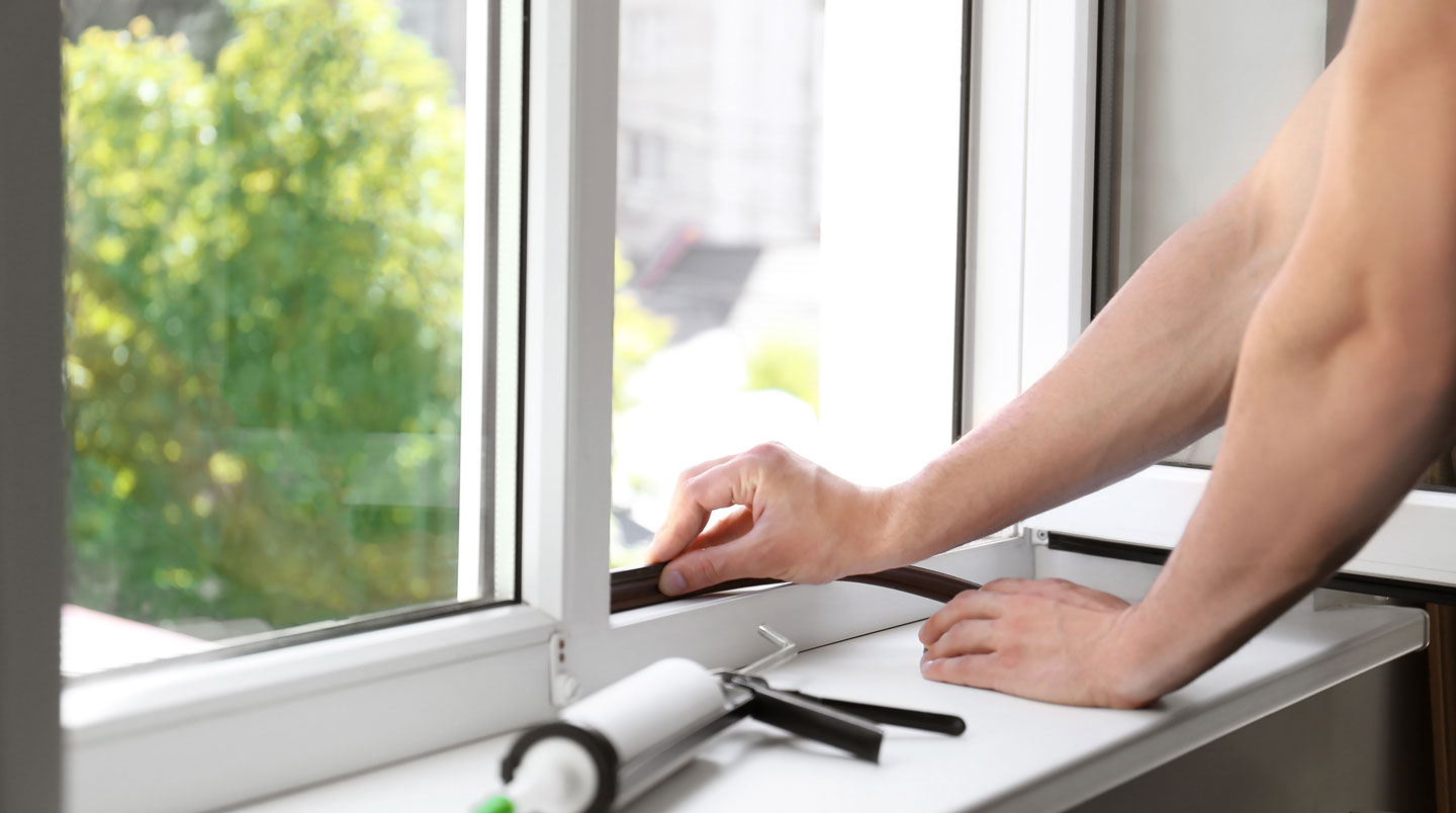 Un installateur professionnel mesure un cadre de fenêtre avec un ruban à mesurer dans un intérieur résidentiel québécois moderne, photographié de profil